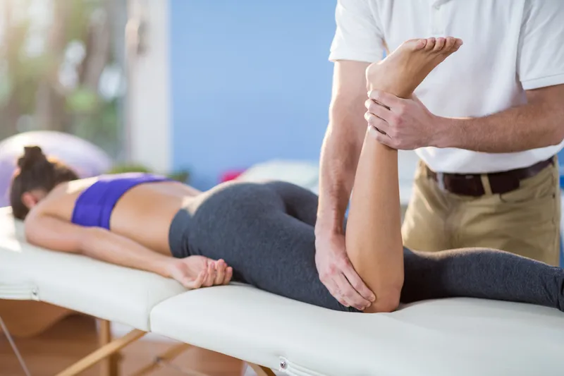 Male physiotherapist giving knee massage to female patient in clinic